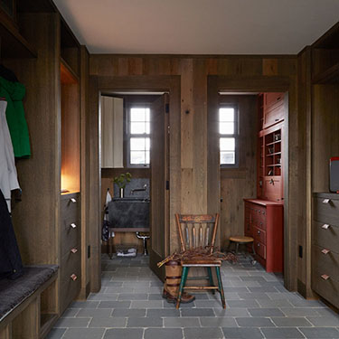 photo of hallway with fumed oak panel walls, 2 open doorways at end. Left shows black sink, right shows cabinets with rust colored milk paint finish