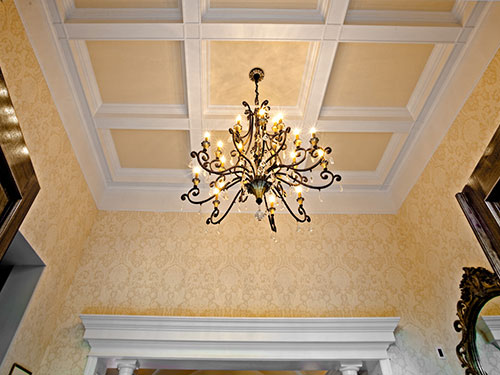 photo of coffered ceiling with white beams, yellow recesses and chandelier hanging from middle