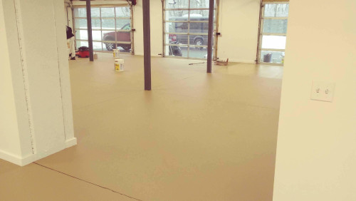 Garage with polymer epoxy floor in light yellow with three garage doors in center back